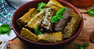 Prato de dolma feitos com folhas de videira, recheados e dispostos em uma tigela de cerâmica, decorados com folhas frescas de hortelã.