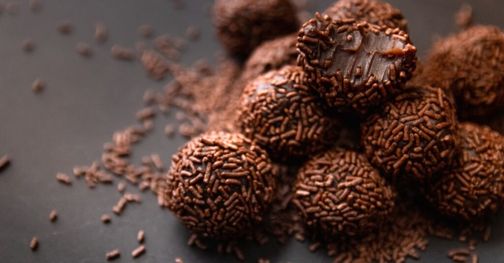 Deliciosos brigadeiros clássicos cobertos com granulado de chocolate em fundo preto, destacando sua textura cremosa e aspecto artesanal.