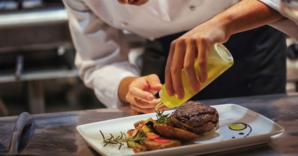 Chef finalizando um prato com azeite, revelando o segredo dos molhos usados para realçar sabor e textura nos restaurantes.
