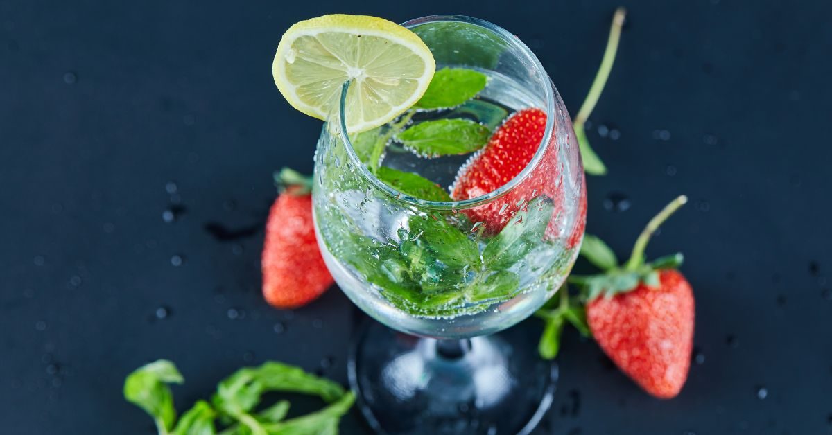 Taça de drink com espumante, decorada com morangos e hortelã.