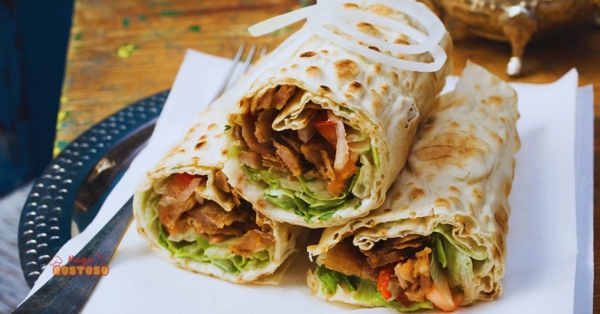 Shawarma enrolado no pão sírio com carne, vegetais frescos e temperos, servido em um prato. Receita tradicional do Oriente Médio